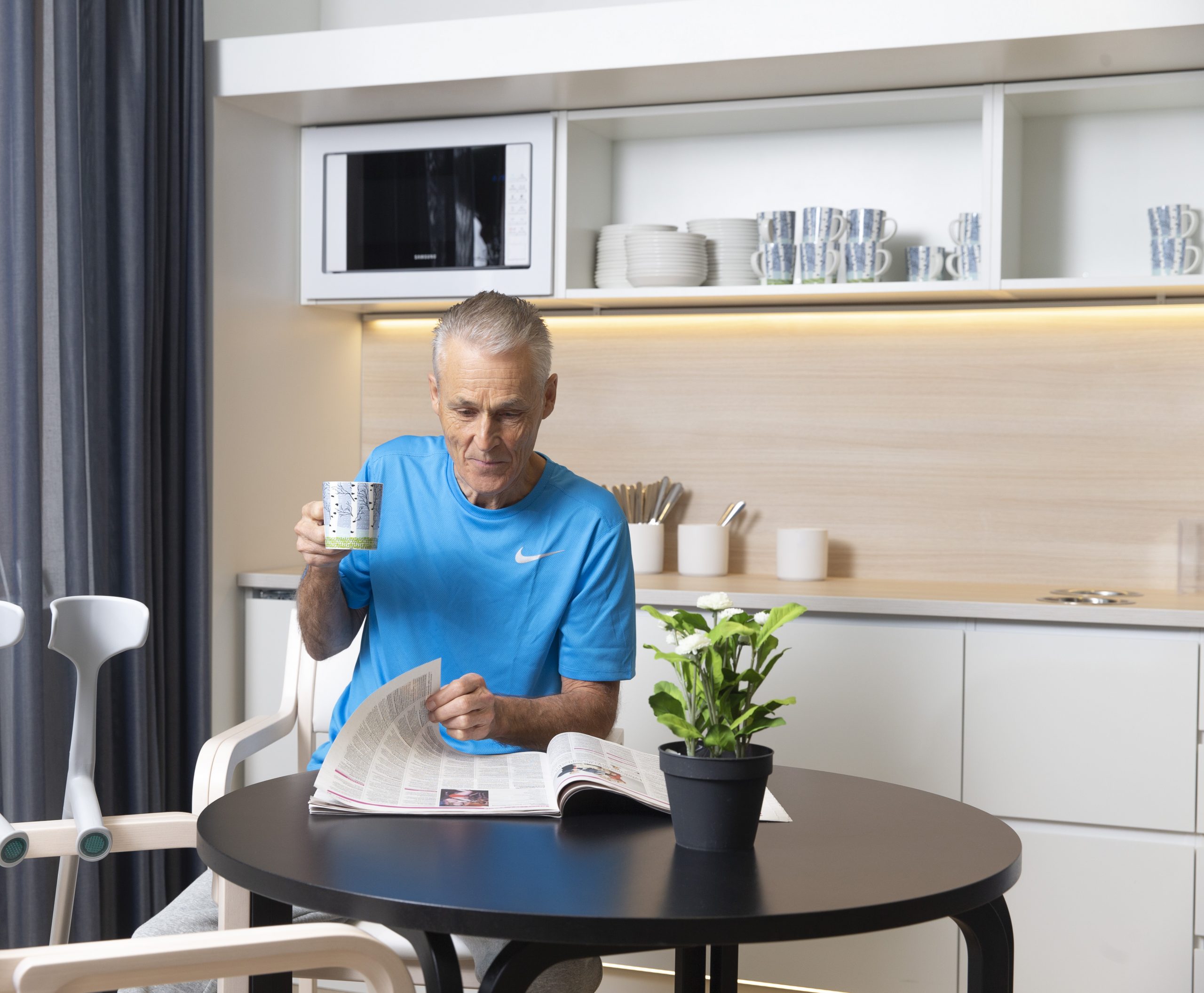 Kuvassa mies juo kahvia ja lukee lehteä.